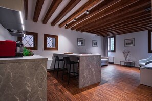 A modern kitchen with a marble island, wooden beams, and a red appliance.
