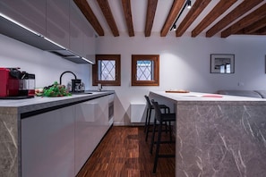 A modern kitchen with a marble countertop, wooden beams, and a small island with bar stools.