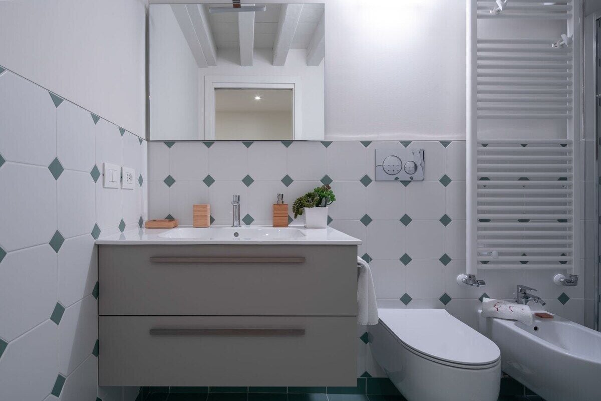 Een badkamer met een wit wastafelmeubel, spiegel en toilet. Er is een handdoekhouder en een plant op het aanrecht.