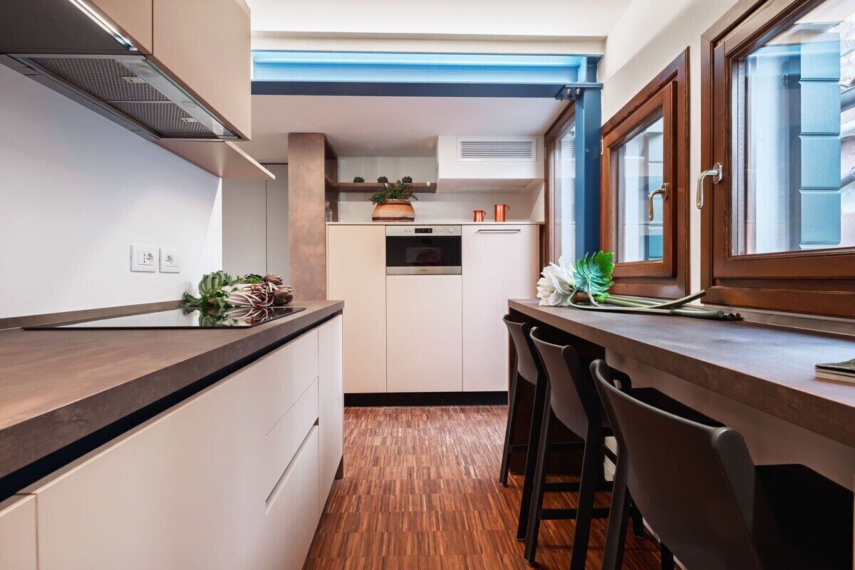 A compact kitchen with a built-in oven, a coffee machine, and a small dining area with a table and chairs.
