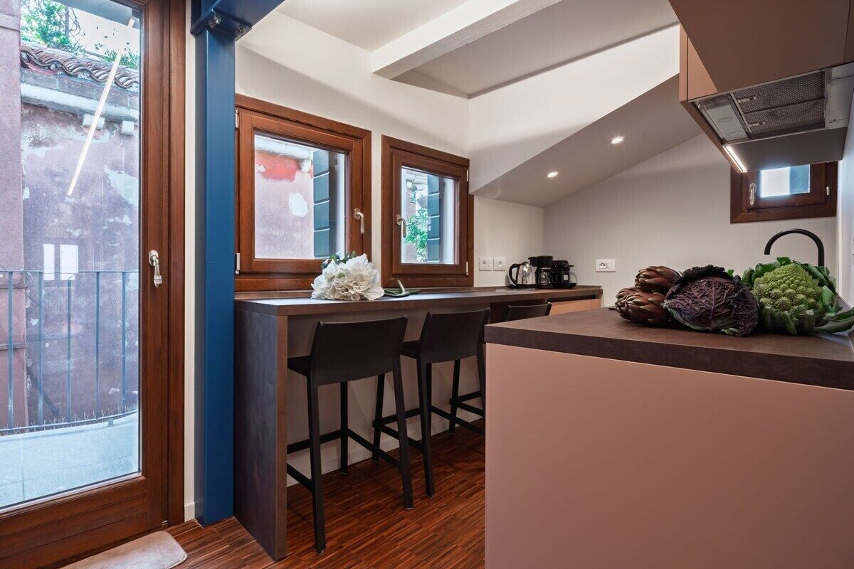 A modern kitchen with a central island, bar stools, and a view of the outside.