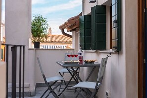 Un balcon avec une table, des chaises, un pot de fleurs et une fenêtre avec des volets verts.