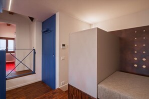 Una habitación con puerta azul, pared blanca con perforaciones circulares y suelo de madera.