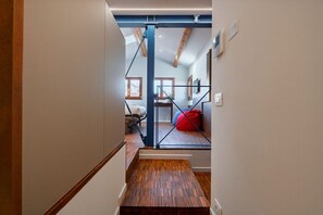 Un couloir étroit doté d’un plancher en bois et d’une poutre bleue en métal apparent.