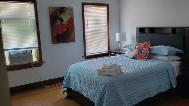 A bedroom with a bed, a nightstand, a lamp, and a window with blinds.