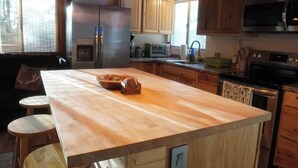 Una cocina con armarios de madera, una isla central con taburetes, electrodomésticos de acero inoxidable e iluminación colgante.