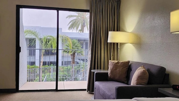 Hotelkamer met een bed, een slaapbank, een lamp en uitzicht op een balkon met palmbomen.