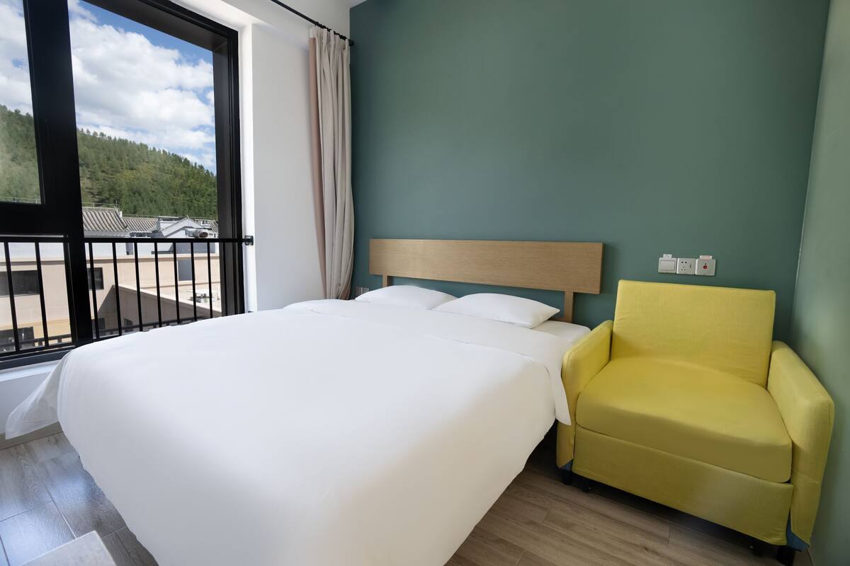 Et hotelværelse med en seng, en gul lænestol, udsigt til en balkon og en grøn væg.