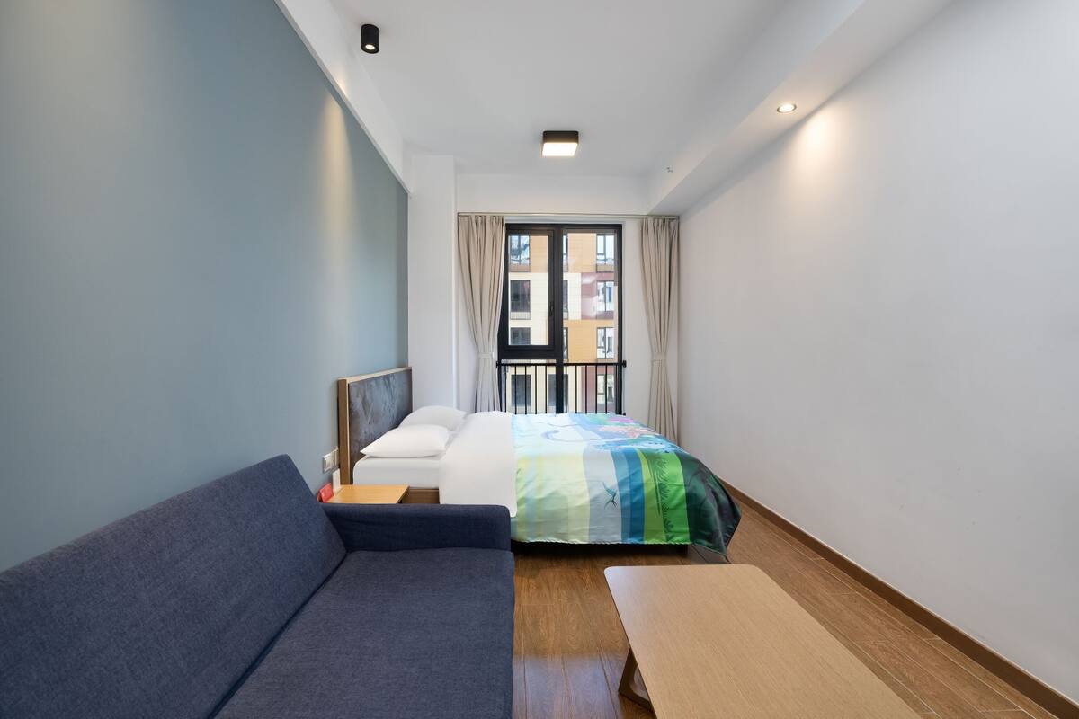 Et lille hotelværelse med en seng, en sofa, et lille bord og et vindue med gardiner.