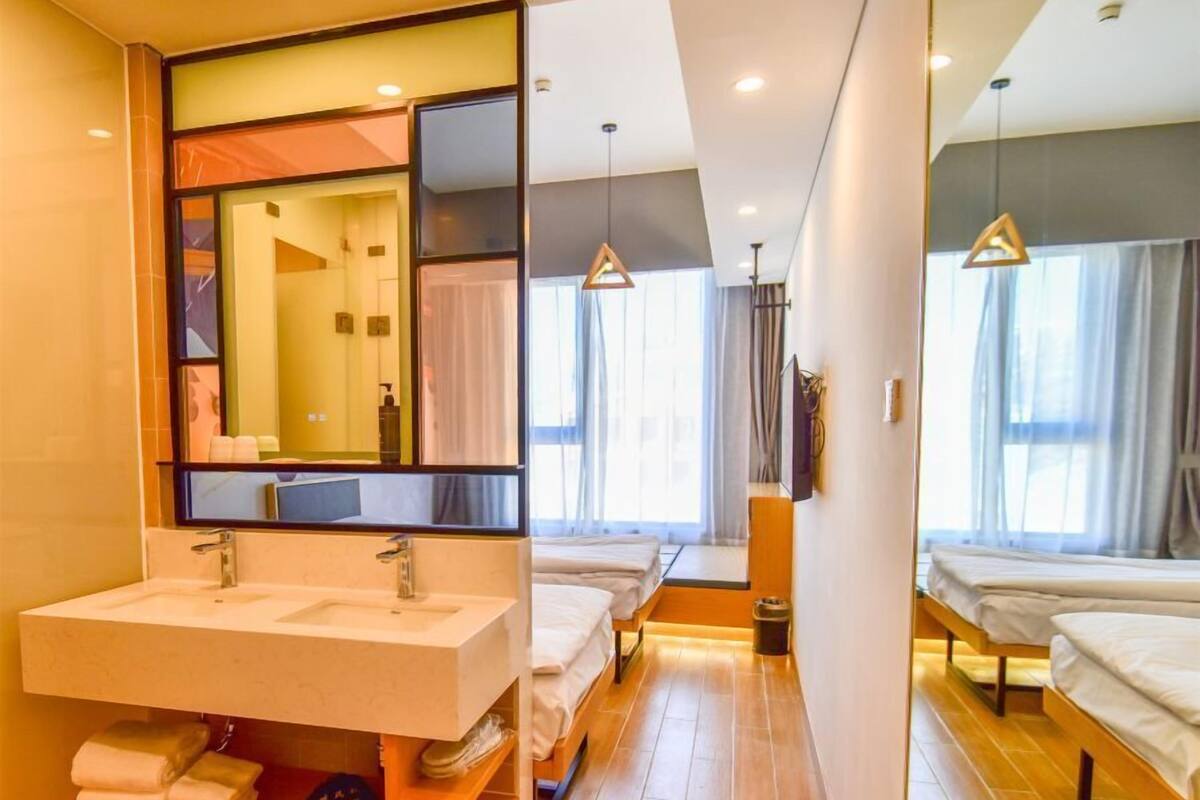 Et moderne hotelværelse med et stort spejl, to senge, trægulv og et badeværelse med vask og håndklædetørrestativ.