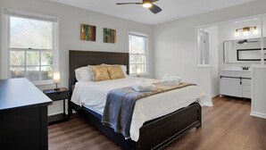 Una camera da letto con un letto, comodini, una ventola a soffitto e un bagno con uno specchio e luci.