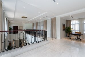 A spacious interior with a marble floor, a balcony with a wrought iron railing, and a dining area with a table and chairs.