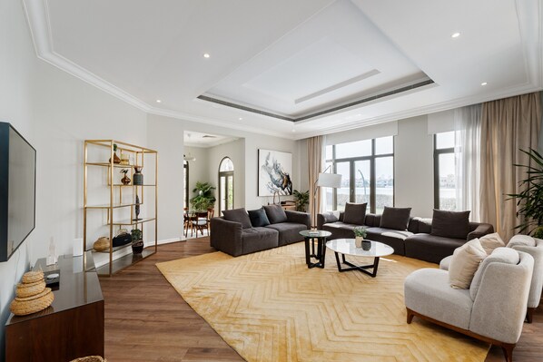 A spacious living room with a large sofa set, a coffee table, and a TV on a wooden console.
