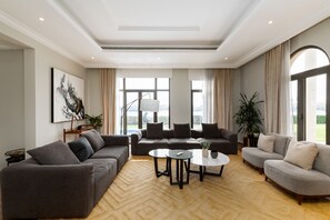 A spacious living room with a large sectional sofa, a round coffee table, and a view of the outdoors through large windows. - Beachfront 6BR Villa w/ Private Pool at the Palm (Dubai)