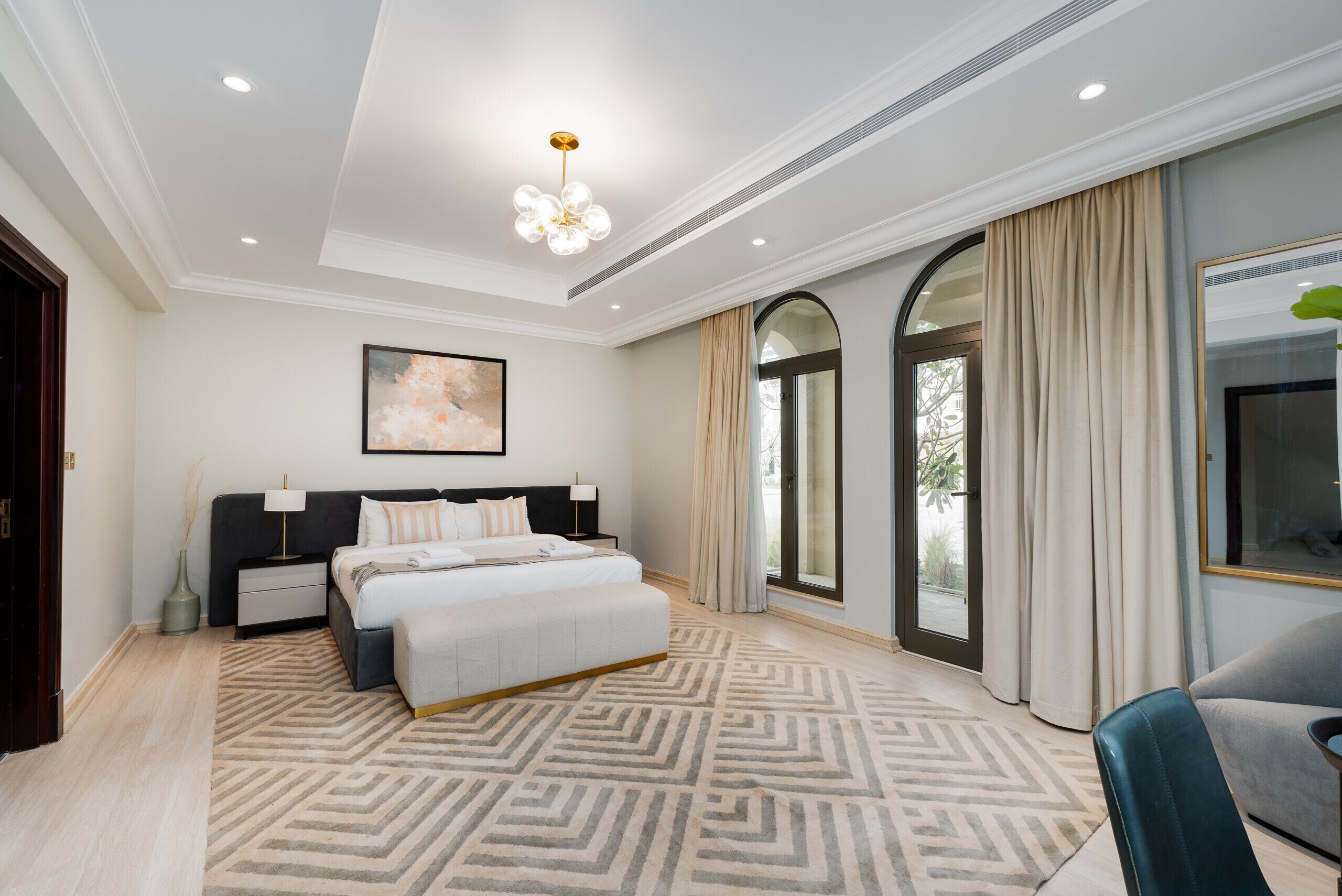 A modern bedroom with a large bed, a nightstand, a bedside table, a floor lamp, and a large window with curtains.