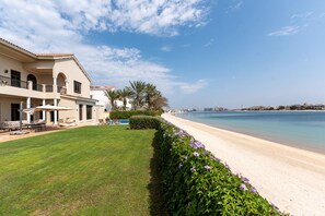 A beachfront property with a well-maintained lawn, a pool, and a view of the sea.