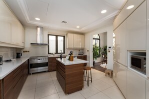 Une cuisine moderne dotée d’un îlot central, d’appareils électroménagers en acier inoxydable et offrant une vue sur l’extérieur.