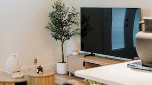 A modern living room with a flat-screen TV, a potted plant, a white vase, and a small round table.