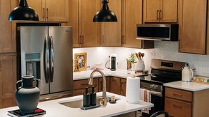 A modern kitchen with wooden cabinets, stainless steel appliances, a central island with seating, and pendant lighting.