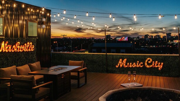 An outdoor seating area with a view of the city skyline, featuring neon signs for 'Nashville' and 'Music City'.