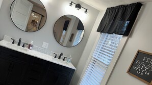Een badkamer met een zwart wastafelmeubel, een ronde spiegel en een plafondlamp.