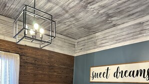 Een slaapkamer met een bed, een bord aan de muur, een houten plafond en een raam met gordijnen.