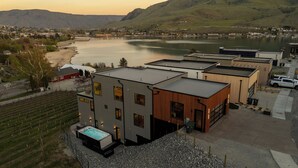 A modern building with a swimming pool, located near a lake with a view of hills. - Ultra Luxury Chelan Lake House w/ Sauna, Steam Room, Cold Plunge, and Hot Tub (Chelan)