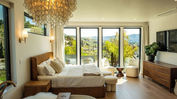 A modern bedroom with a large bed, a sitting area, a bathtub, and a view of the outdoors. - Ultra Luxury Chelan Lake House w/ Sauna, Steam Room, Cold Plunge, and Hot Tub (Chelan)