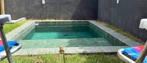 Una piscina con cerramiento de madera, una botella de champán y dos sillas de descanso.