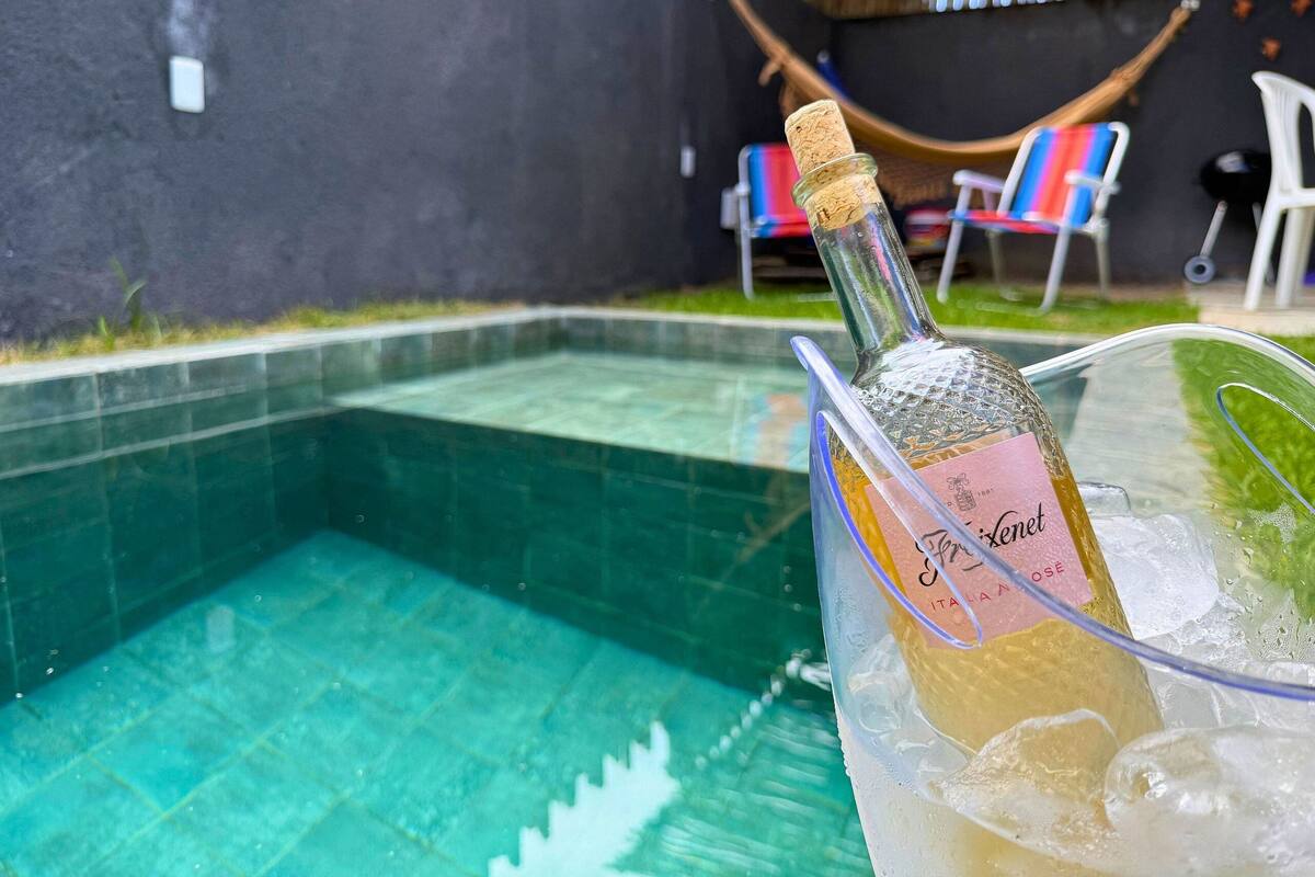 A bottle of champagne in a glass with ice cubes, placed near a swimming pool.