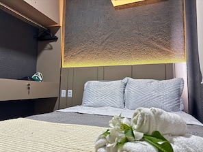 A hotel room with a bed, a bedside table, a wall-mounted light, and a towel on the bed. - MHV Milagres - Studio Guadalupe 05 (Passo de Camaragibe)