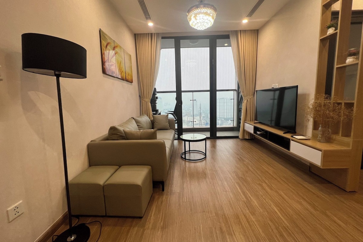Un salon moderne avec un canapé, un téléviseur et une grande fenêtre donnant sur la ville.