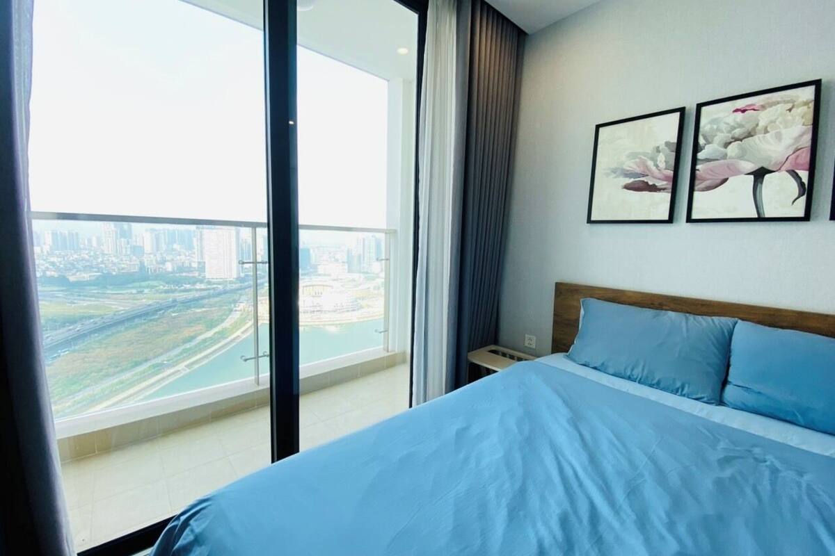 Une chambre avec un grand lit, une table de chevet et une vue sur le paysage urbain, visible depuis un balcon.