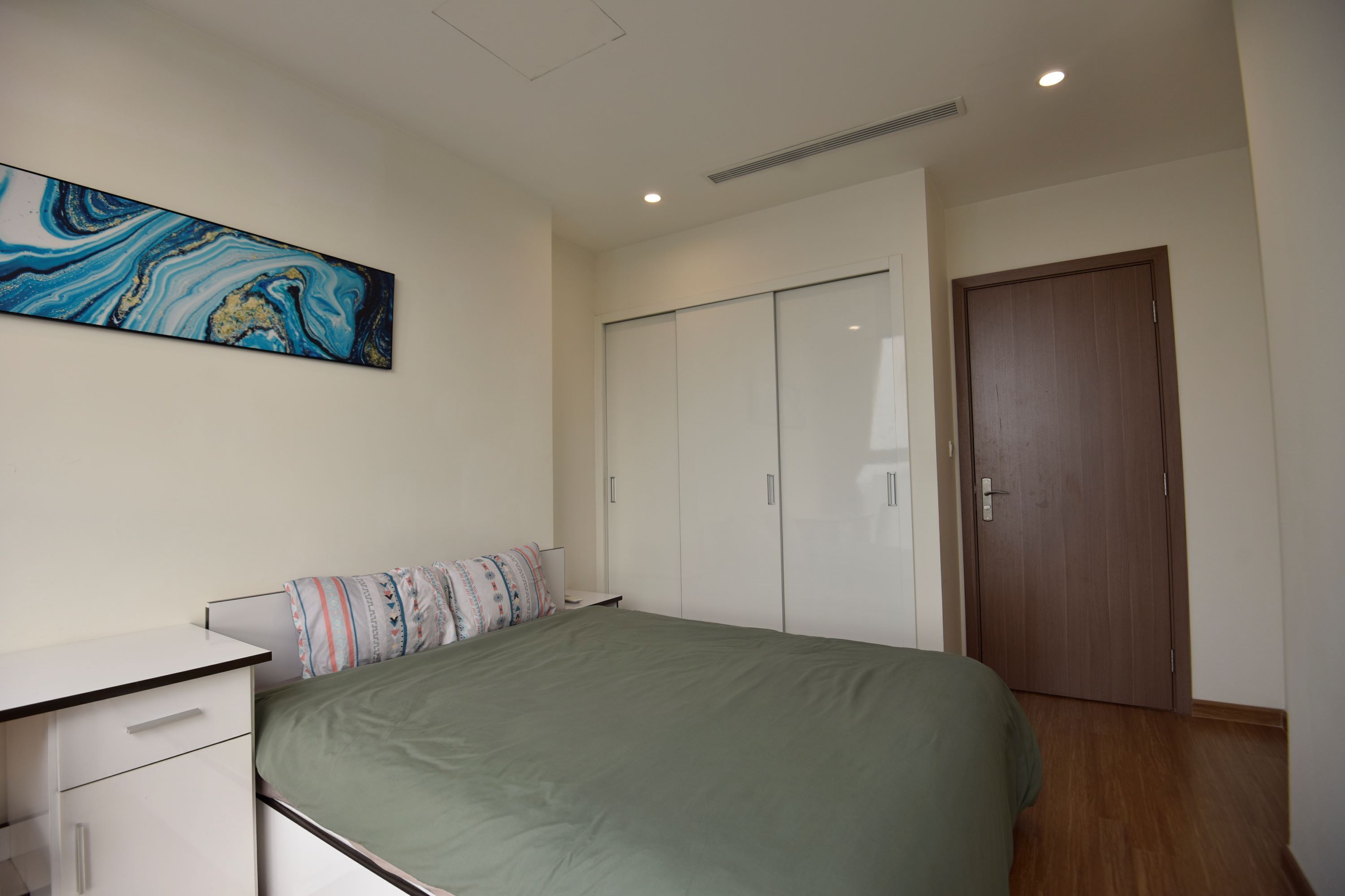 A bedroom with a bed, a desk, a wardrobe, and a painting on the wall.