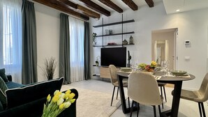Uma sala de estar moderna com área de jantar, apresentando uma TV de tela plana, uma mesa de jantar posta para quatro pessoas e um sofá com um buquê de tulipas.