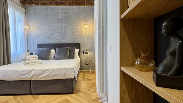 Quarto moderno com cama grande, duas luminárias de cabeceira, cabeceira de madeira e uma escultura em uma prateleira.