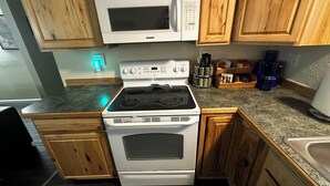 Una cocina con gabinetes de madera, estufa blanca, microondas y encimera de granito.