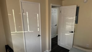 Un pasillo con dos puertas blancas, suelo de madera oscura y pared de color claro.