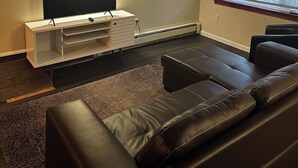 Una sala de estar con un televisor de pantalla plana, un mueble blanco para equipo multimedia, un sofá de cuero marrón, una alfombra y una obra de arte colgada en la pared.