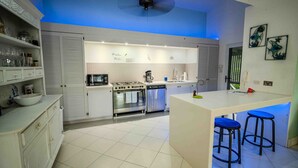 A modern kitchen with white cabinets, a central island with stools, a stove, oven, and dishwasher.