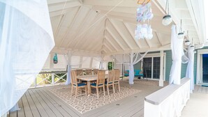 A covered outdoor dining area with a wooden table and chairs, a patterned rug, and a white canopy.