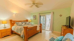 A bedroom with a bed, two bedside lamps, a ceiling fan, a television, and a sliding glass door leading to an outdoor area.
