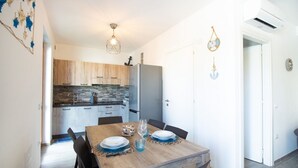 A modern kitchen with wooden cabinets, a grey refrigerator, and a dining area with a wooden table set for two. - Villa Cycas by All4sardinia  (villasimius)