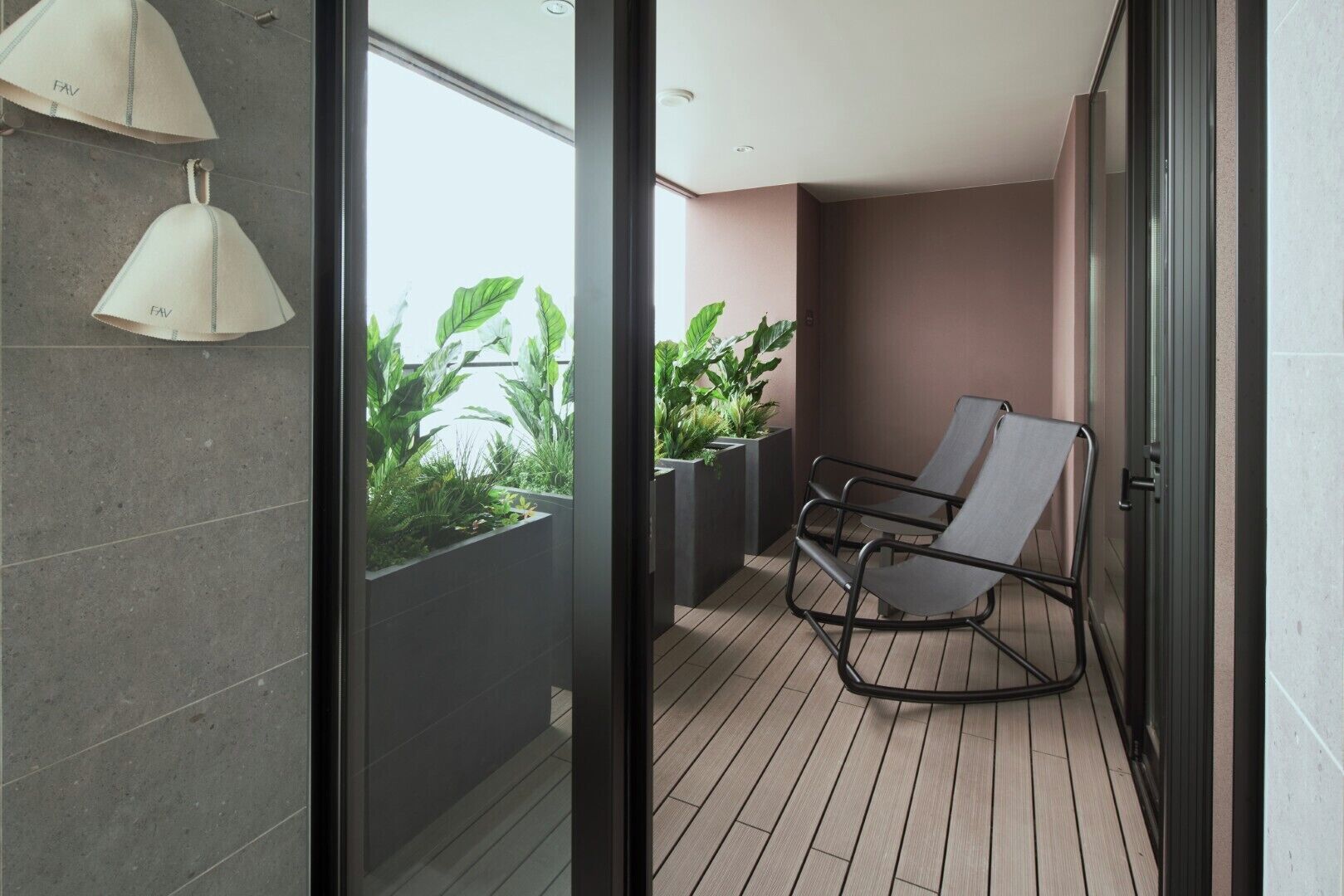 A modern balcony with a wooden floor, a metal chair, and potted plants.