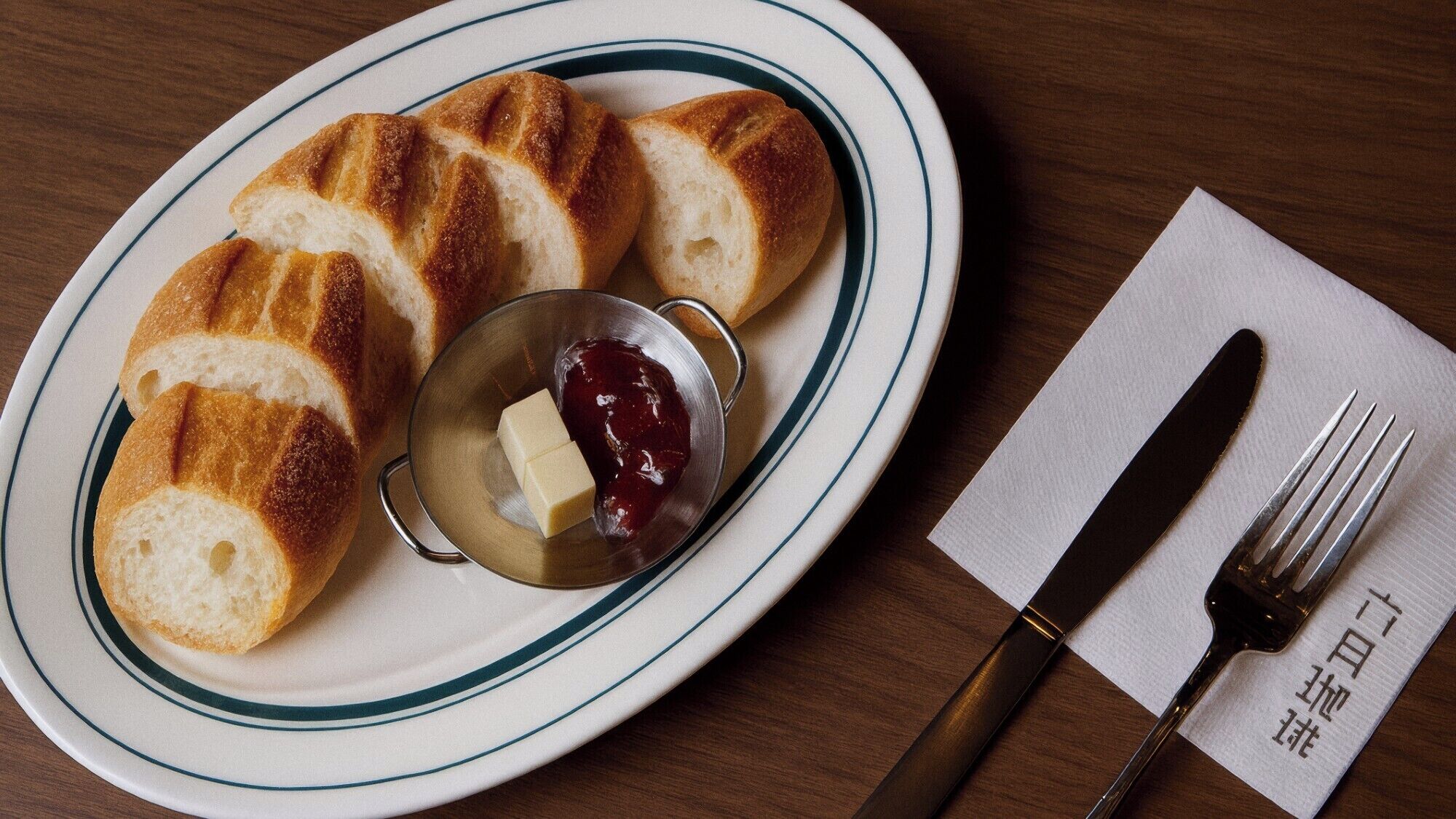 Een bord met croissants, jam en boter, een mes en een vork op een servet.