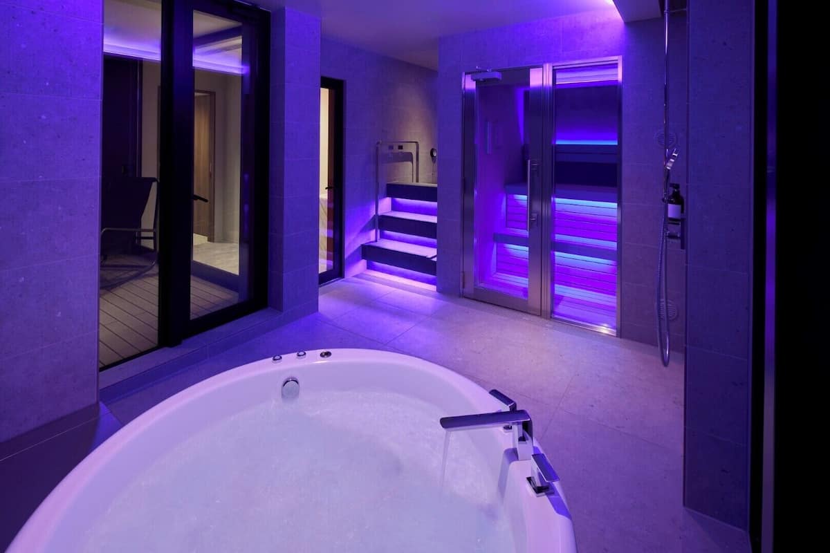 A modern bathroom with a large bathtub, a shower area, and a glass-enclosed staircase.