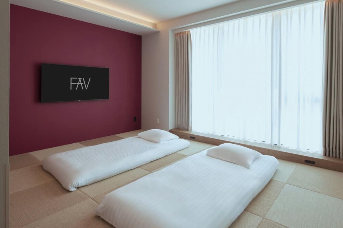 A hotel room with two beds, a TV on the wall, and large windows with curtains.