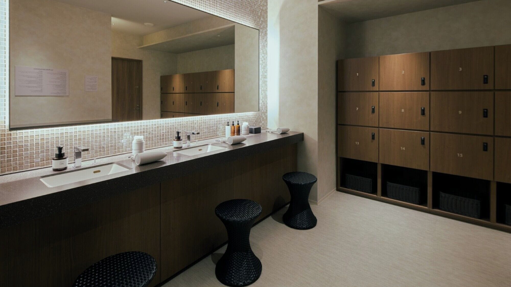 A modern bathroom with a large mirror, a sink, and a row of wooden lockers.
