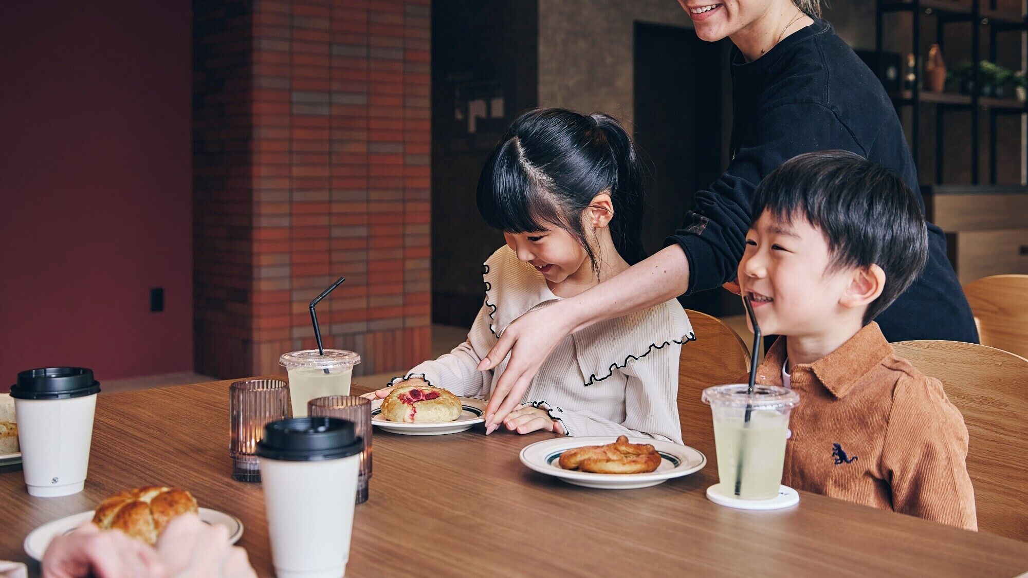 A family dining at a table with coffee cups, a plate of food, and a child reaching for a pastry.