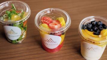 Tres vasos de plástico transparente con tapas, cada uno conteniendo frutas diferentes y con un logotipo.